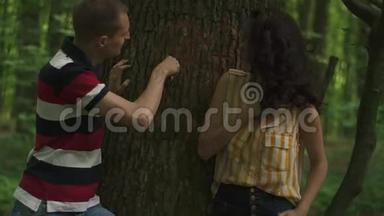 爱情中的年轻夫妇在树上雕刻的一颗心的特写。 绿泉森林背景